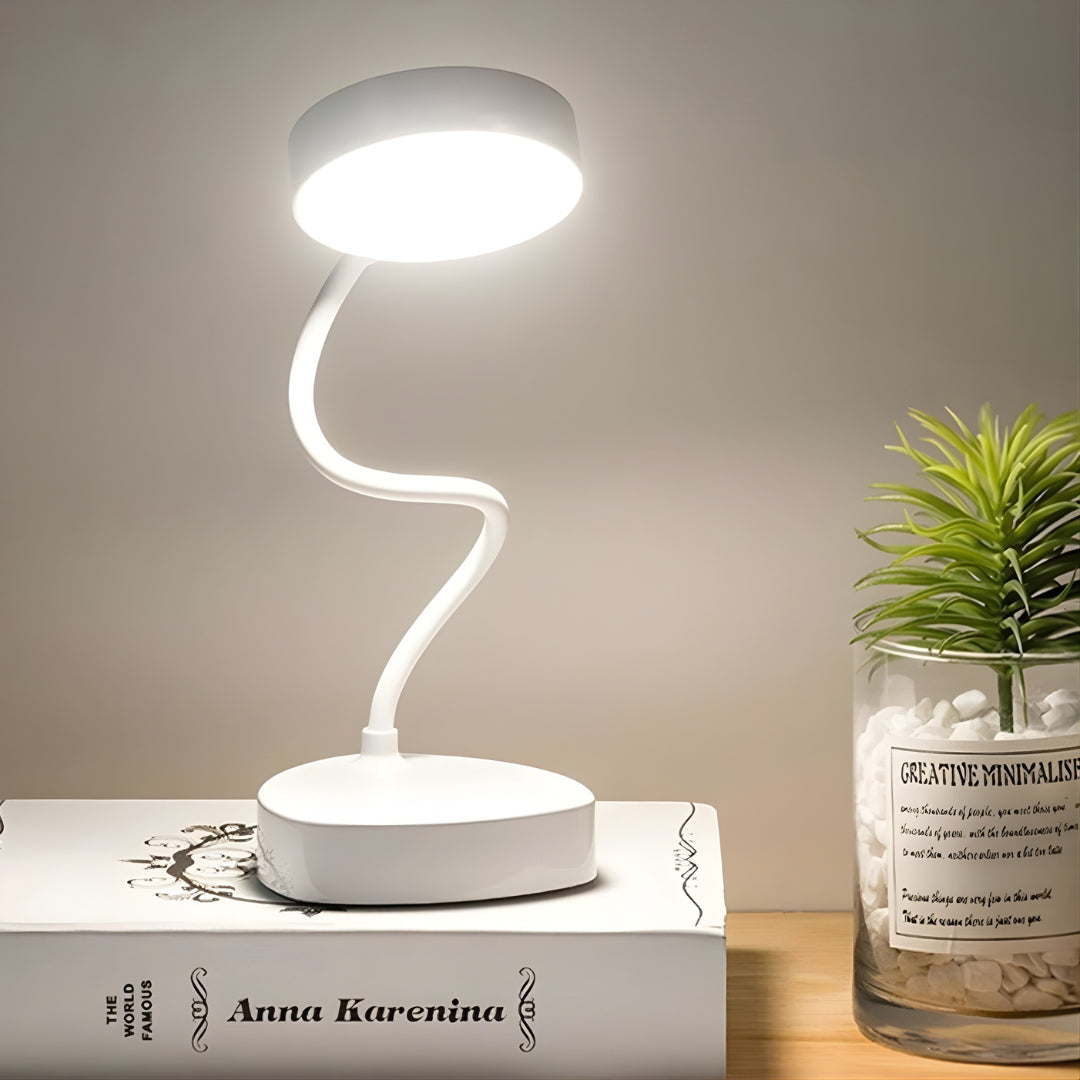 White LED desk lamp on a book with a plant in the background