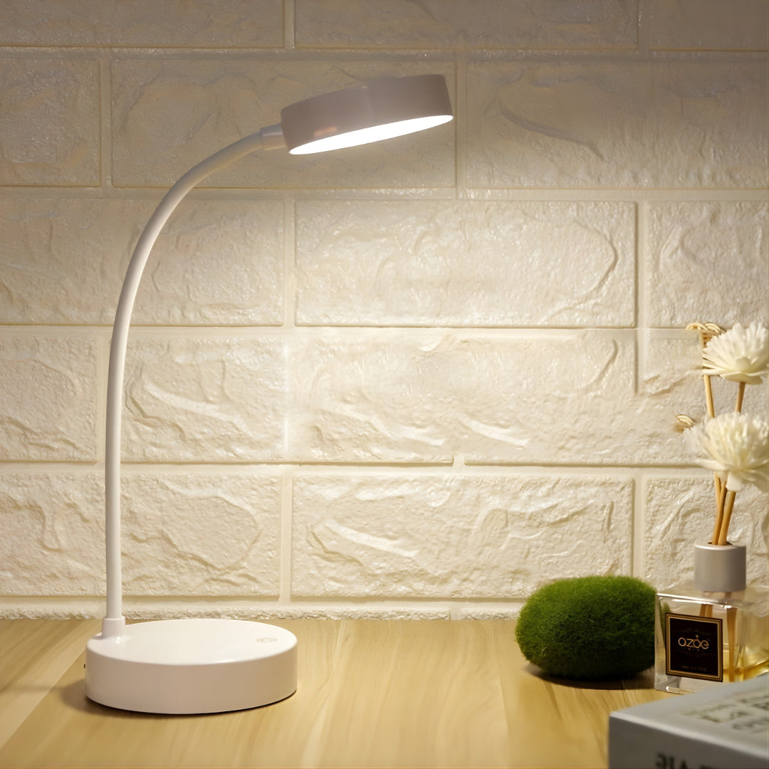 White LED desk lamp on a wooden surface with a decorative plant and vase in the background.