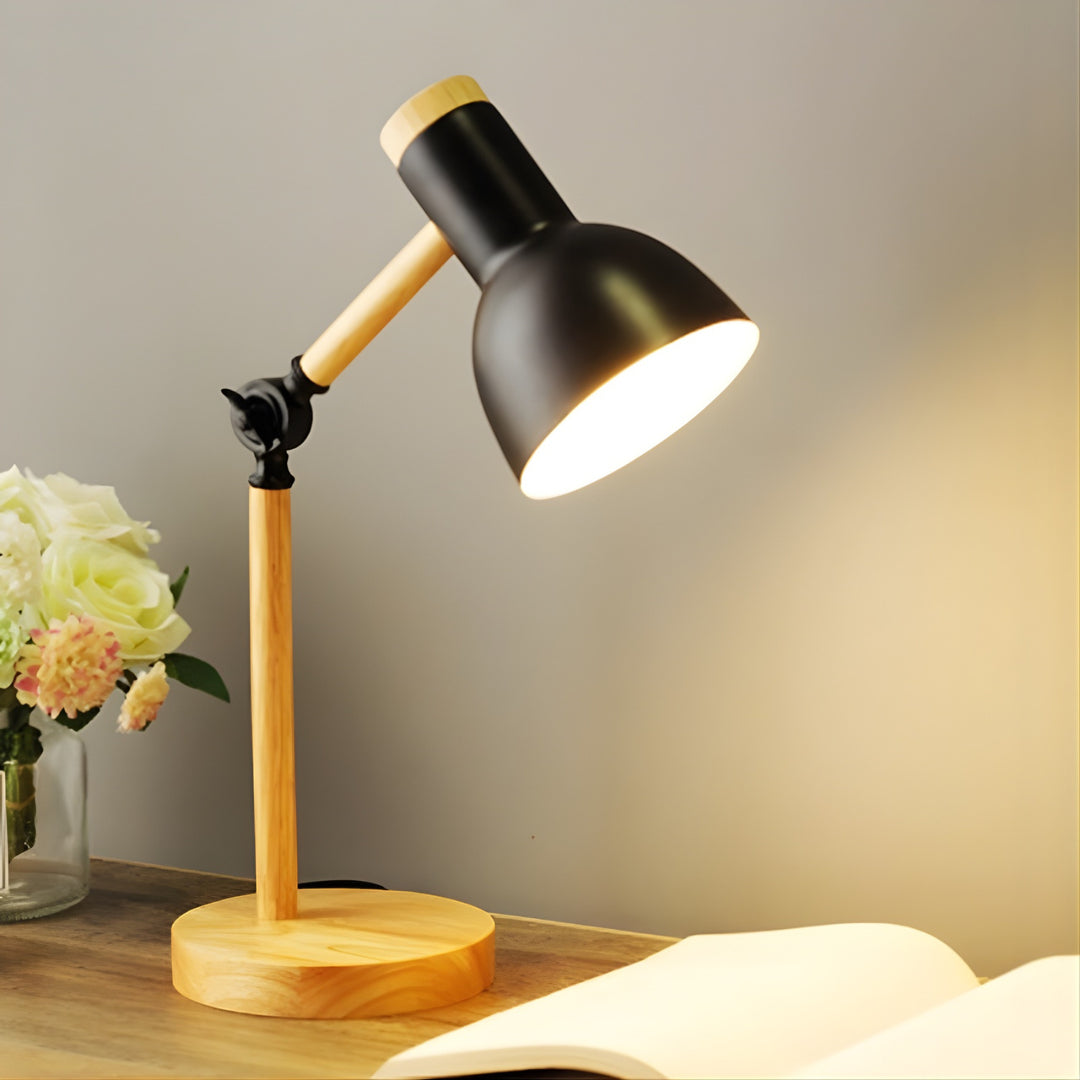 Table lamp with wooden base and black adjustable head on a desk with flowers and book.