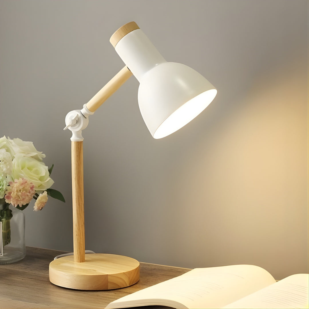 Table lamp with wooden base and white shade on a desk with flowers and an open book.