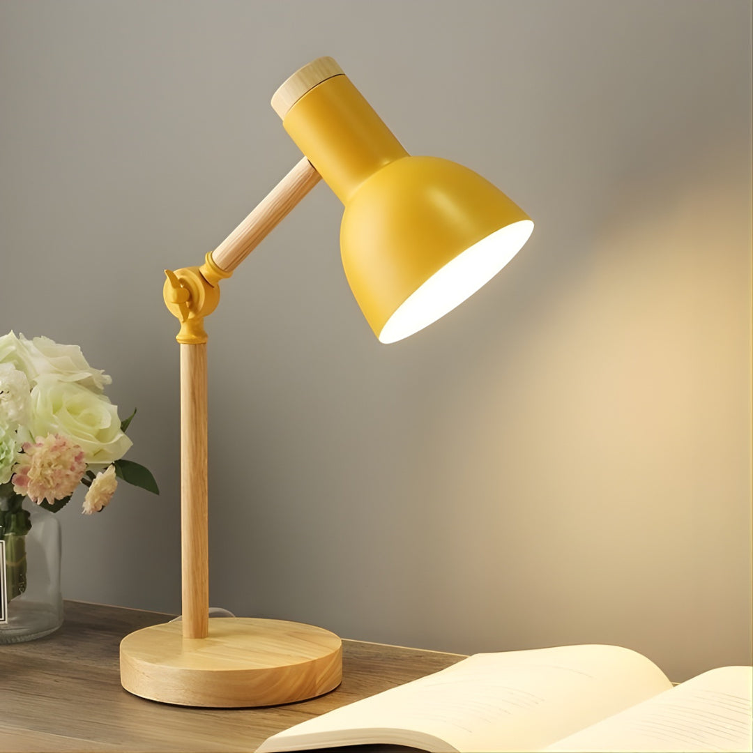 Yellow desk lamp on a wooden base with a soft glow, placed on a surface with flowers and an open book.