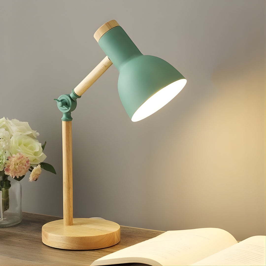 Green and wooden desk lamp on a table with flowers and a book in the background