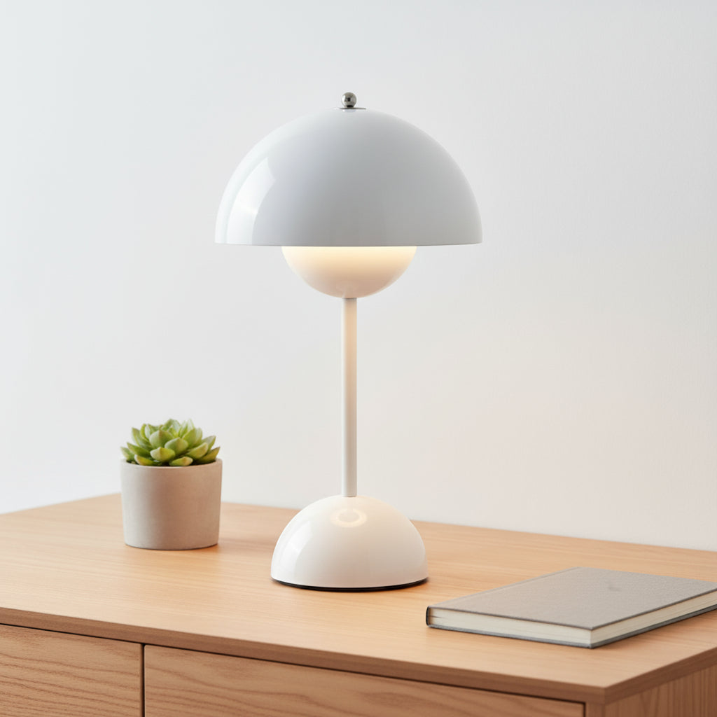 White table lamp on a wooden surface with a small plant and notebook in the background