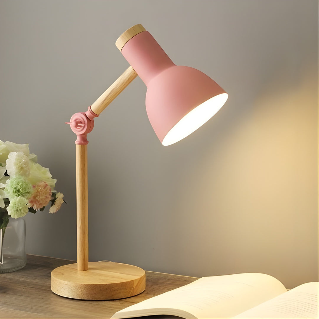 Pink and wooden desk lamp on a surface with a book and flowers in the background.