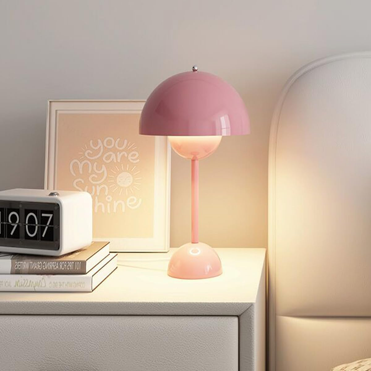 Pink table lamp on a nightstand with a clock and framed picture in the background