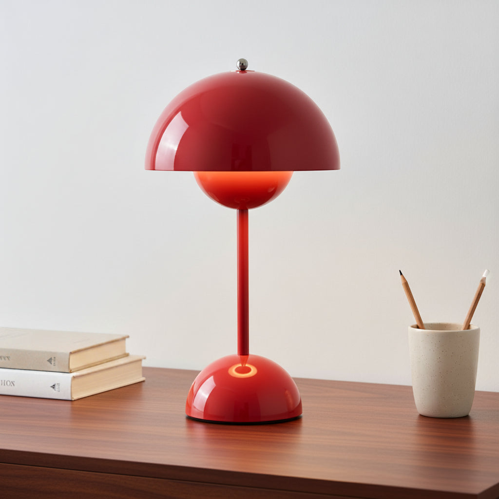 Red table lamp on a wooden surface with books and a cup in the background